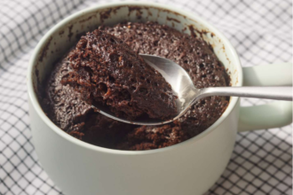 Metal spoon scooping rich, moist chocolate mug cake from a pale green ceramic mug resting on a checkered napkin