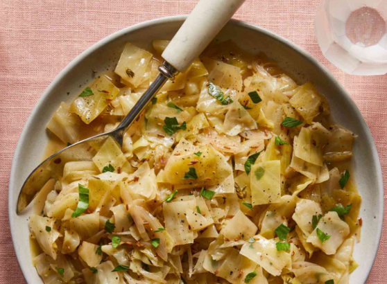 Tender braised cabbage cooked with onions, garlic, butter, and herbs in a savory broth, garnished with fresh parsley.