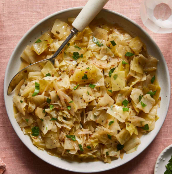 Tender braised cabbage cooked with onions, garlic, butter, and herbs in a savory broth, garnished with fresh parsley.