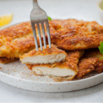 Crispy golden chicken cutlets served with lemon wedges and fresh herbs on a white plate.