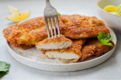 Crispy golden chicken cutlets served with lemon wedges and fresh herbs on a white plate.