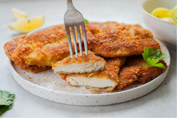 Crispy golden chicken cutlets served with lemon wedges and fresh herbs on a white plate.