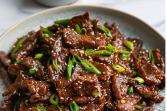 Crispy Mongolian beef coated in a glossy sweet and savory sauce, served with green onions and steamed rice.